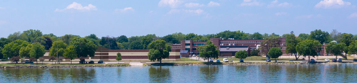 Front facing rendering of a redeveloped waterfront water treatment campus with brick utility buildings, walking paths, trees, landscaped green space, a rocky shoreline and Lake Winnebago in front