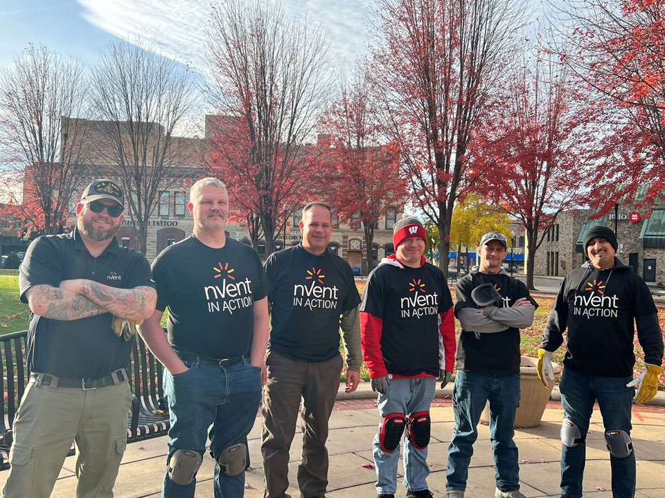 A group of 6 volunteers from NVent  pose for a picture downtown Oshkosh as they work on planting tulip bulbs in Opera House Square