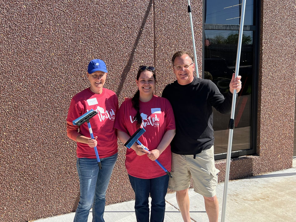 Three volunteers pose for a picture while washing windows at our Parks office on Witzel on a beautiful Spring day